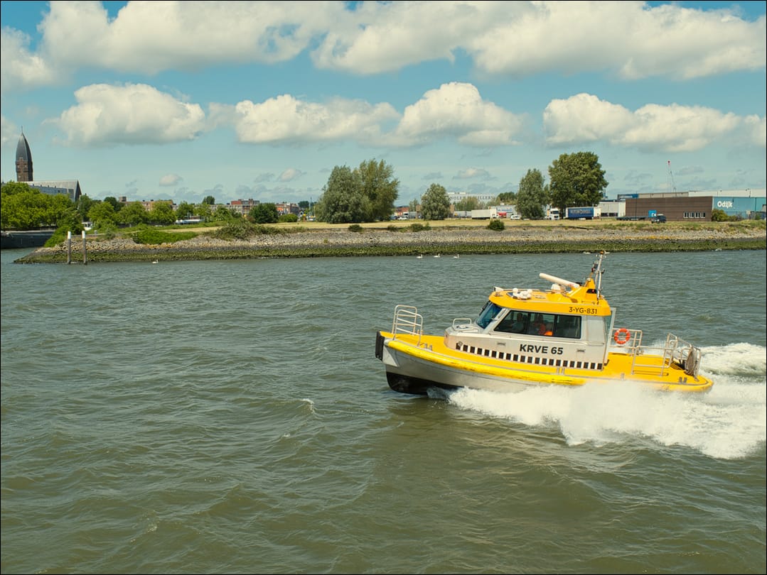 Yellow boat leaves a wake as it speeds along the estuary.